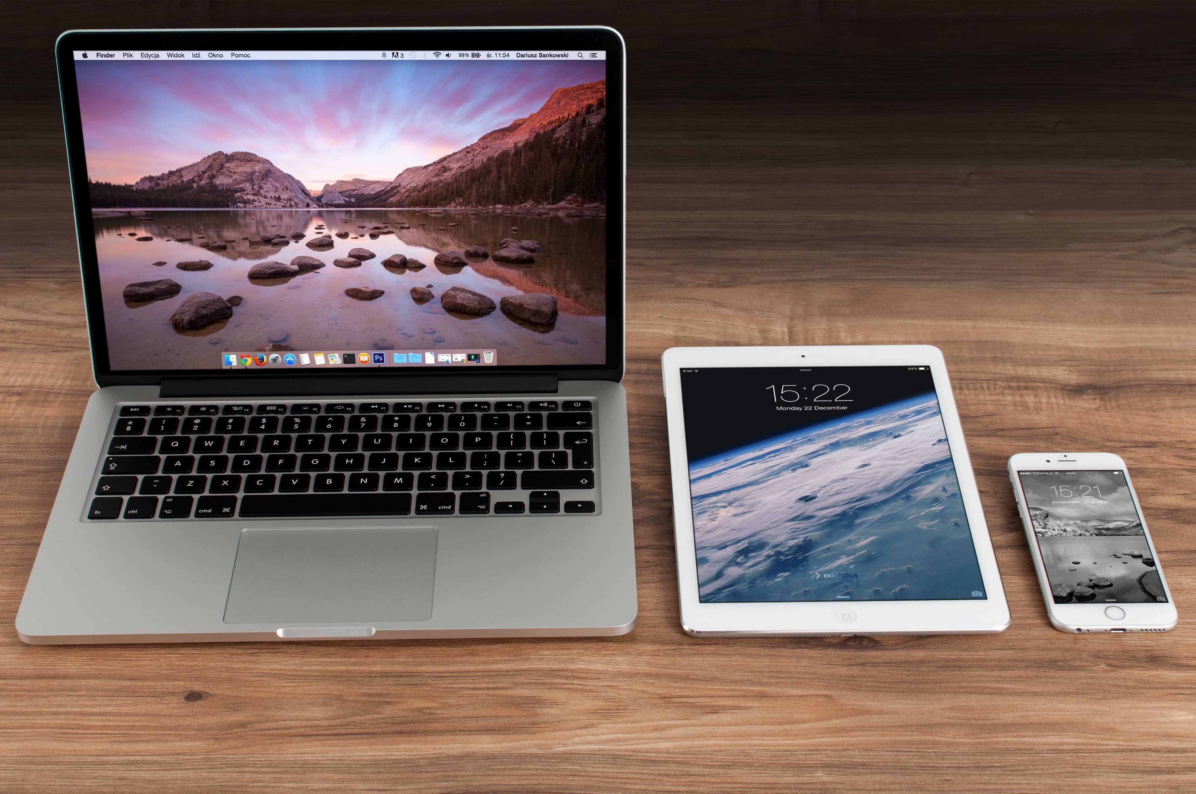 MacBook, iPad und iPhone nebeneinander auf einem Holzschreibtisch