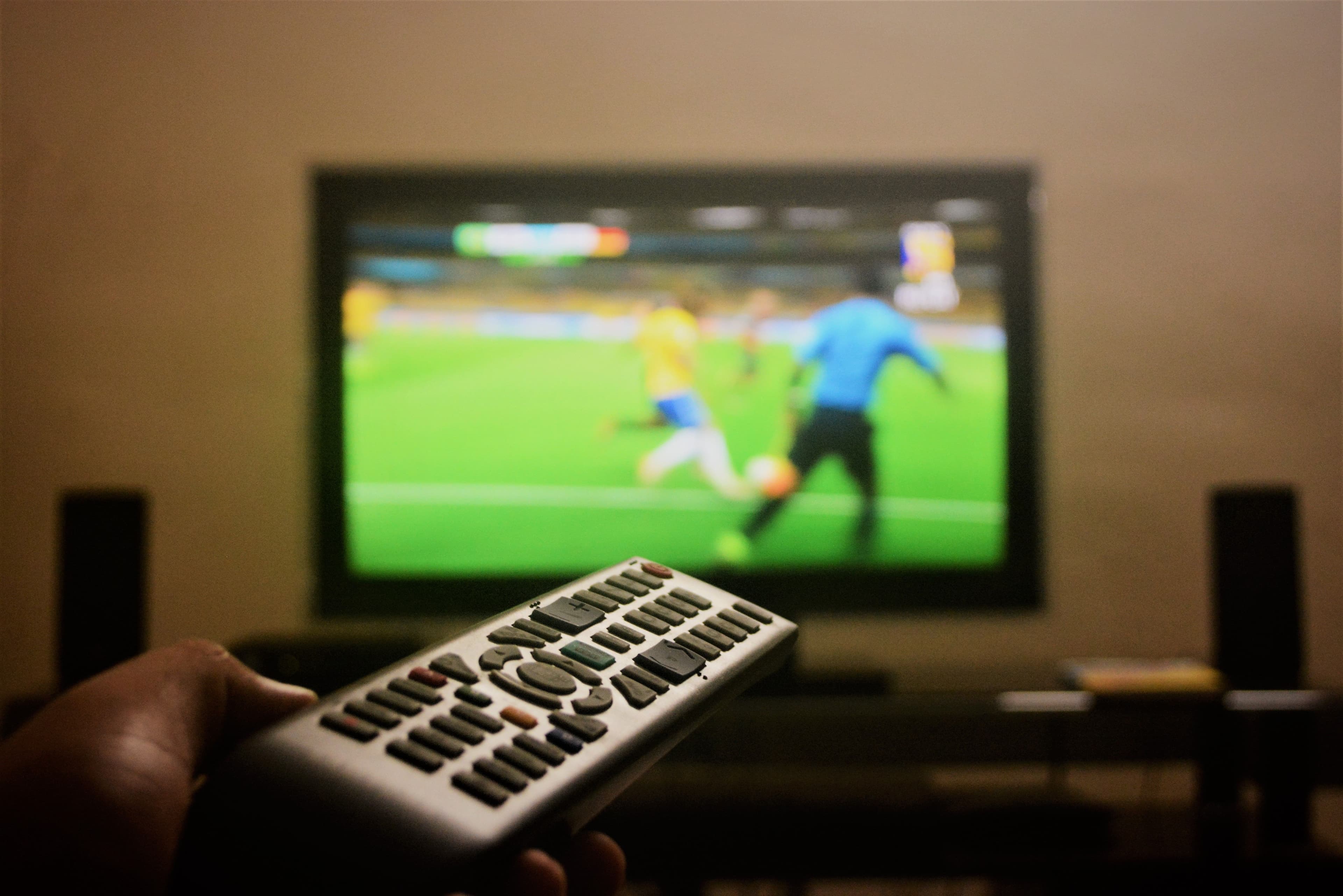 Person schaut Live-Sport auf einem großen Fernseher mit einer Fernbedienung